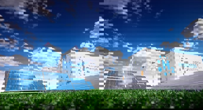 solceller, vindmølle og Hydrogen H2 foran blå himmel med skyer