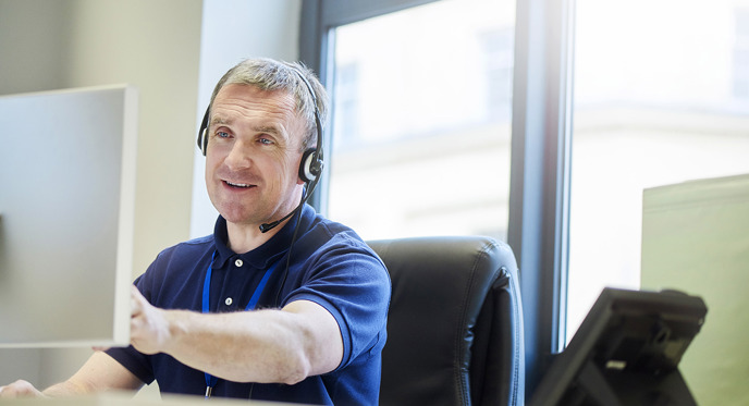 Smilende person sidder bag skærm med headset på