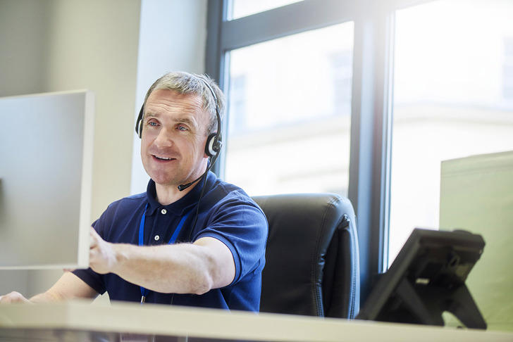 Smilende person sidder bag skærm med headset på