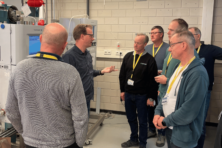 Gruppe af teknikere under en praktisk service-træning foran et Yokogawa GC8000-anlæg, hvor en instruktør forklarer funktioner og anvendelse af udstyret.